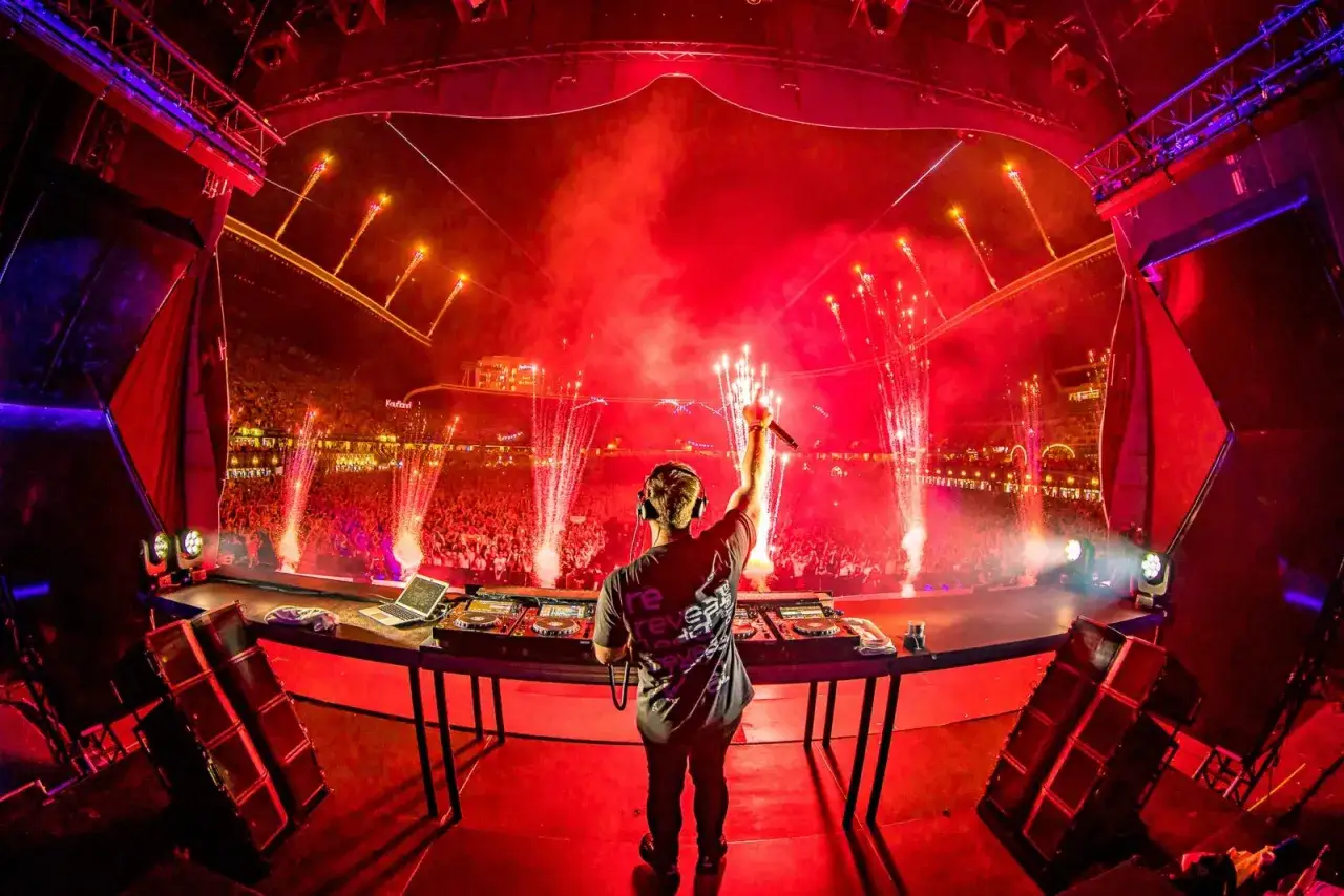 DJ Hardwell na scenie w Polsce, rozświetlonej fajerwerkami i czerwonymi światłami, przed tłumem fan&oacute;w.