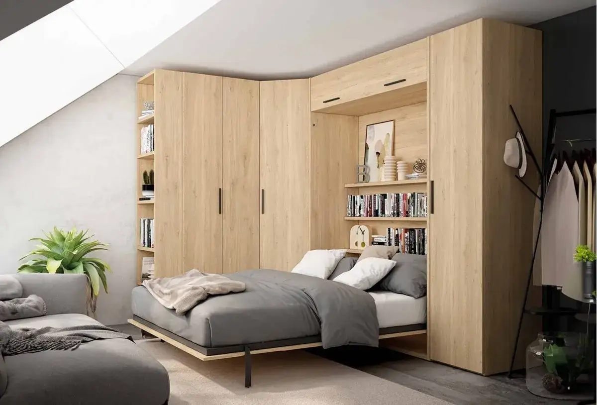 Habitación moderna con sofá gris y cama desplegada de un somier abatible vertical integrado en armarios de madera clara.
