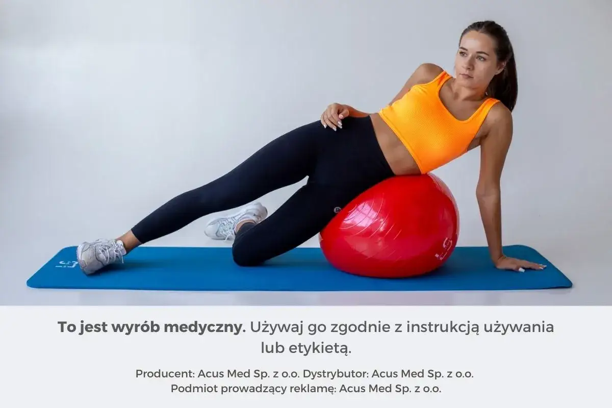 Kobieta wykonuje ćwiczenia z piłką rehabilitacyjną, leżąc na macie.