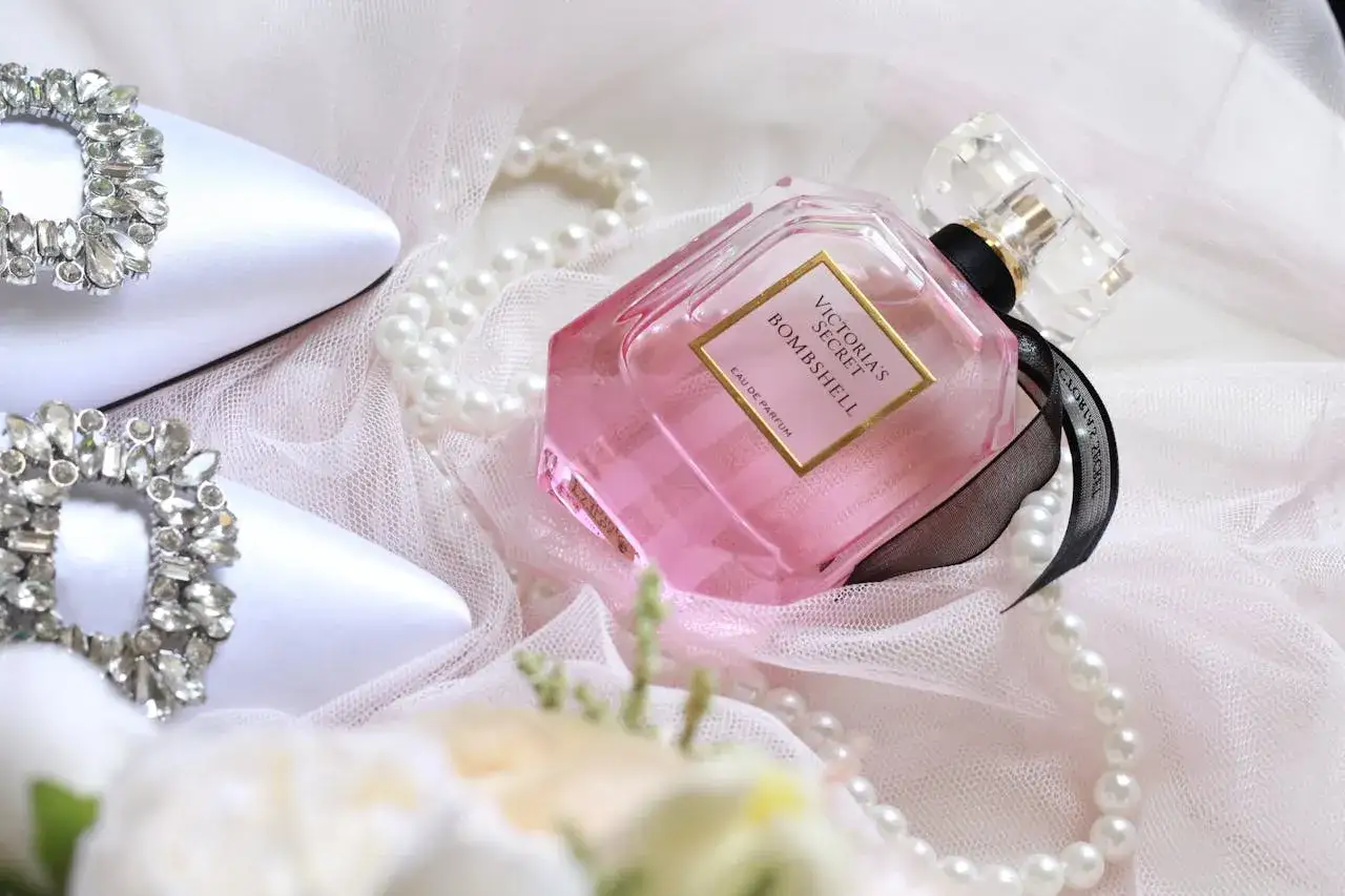 Elegancka kompozycja z różowym flakonem perfum Victoria's Secret Bombshell, biżuterią na butach i perłami. Trwałość perfum oznaczenia są kluczowe.