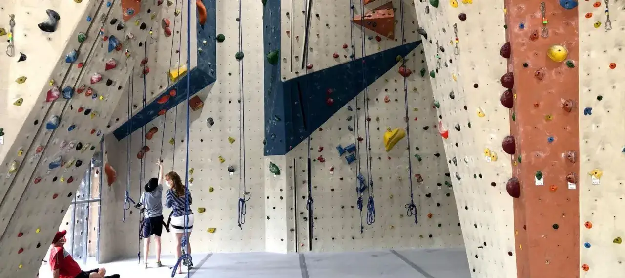 Bunte Griffe an einer Kletterwand, bereit f&uuml;r rotpunkt klettern. Zwei Personen bereiten sich vor, w&auml;hrend eine dritte Person unten sitzt.