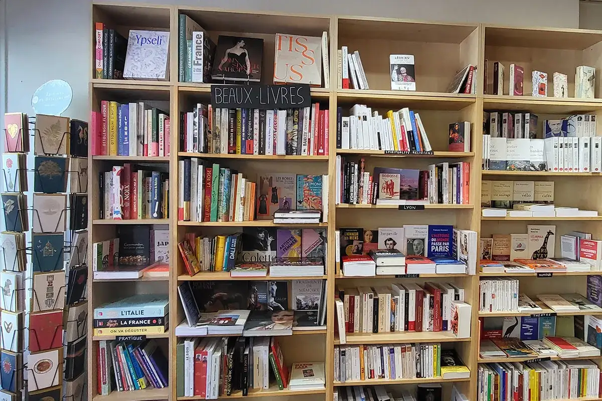 Étagères remplies de livres d'histoire, de beaux livres et de cartes postales. Des titres variés sur l'art, la cuisine et les voyages.