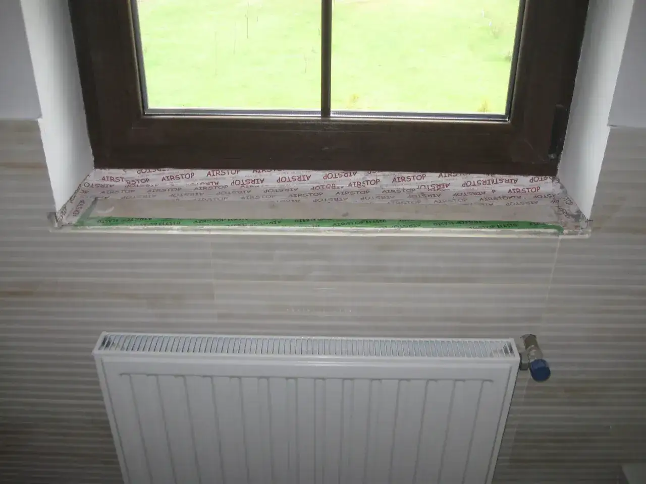 Parapet z płytek wewnątrz, przygotowany do montażu. Pod oknem biały grzejnik.