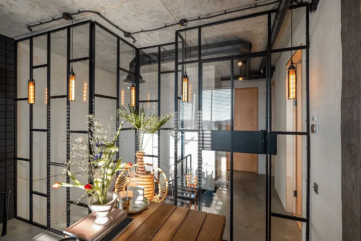 Elegantes tipos de cerramientos interiores de cristal y metal negro, con lámparas colgantes y un arreglo floral.