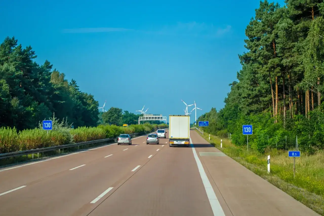 Autostrada w Europie z wiatrakami w tle. Samochody i ciężarówka jadą drogą, a znaki wskazują prędkość 130 km/h.