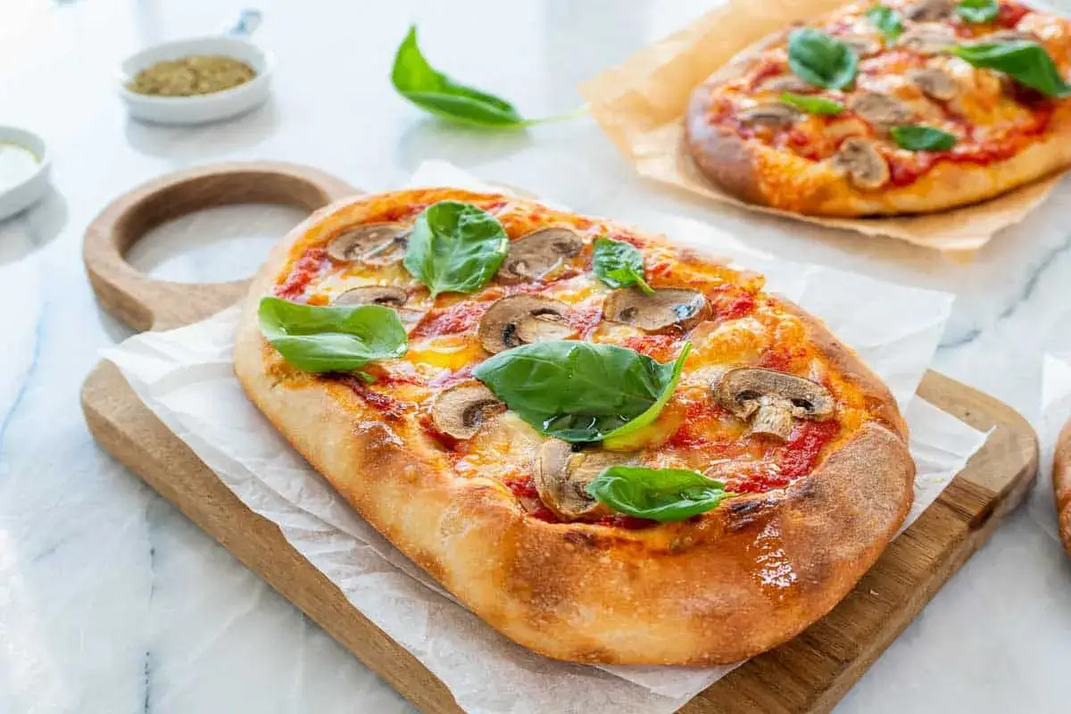Pyszna pinsa co to? To lekka, chrupiąca pizza z pieczarkami i bazylią, podana na desce.