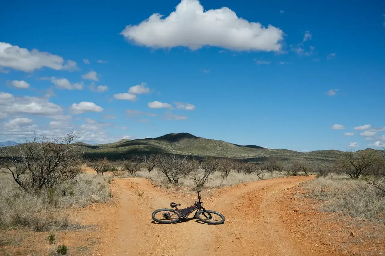 A lone bike rests at a fork in a dusty desert path, hinting at the start of a challenging bike race across America.