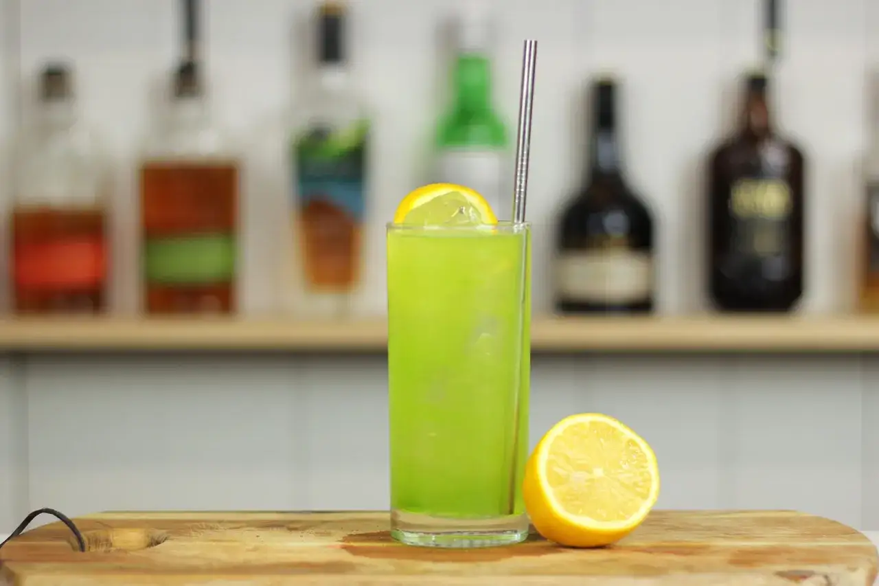 Zielony drink z plasterkiem cytryny, metalową słomką i połówką cytryny obok. Czy to Long Island Iced Tea czy Tokyo Tea?