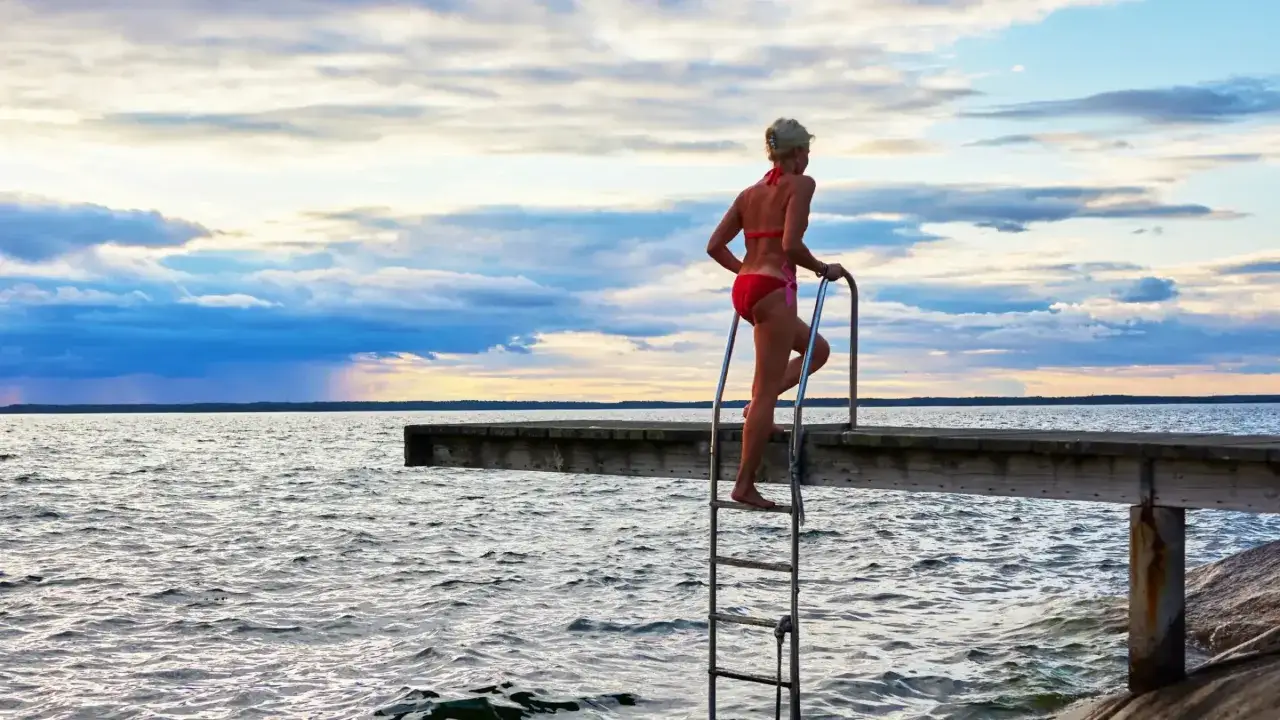 Kvinna i r&ouml;d bikini kl&auml;ttrar upp f&ouml;r badstegen vid en brygga. En avkopplande stund vid ostholmen bastu.