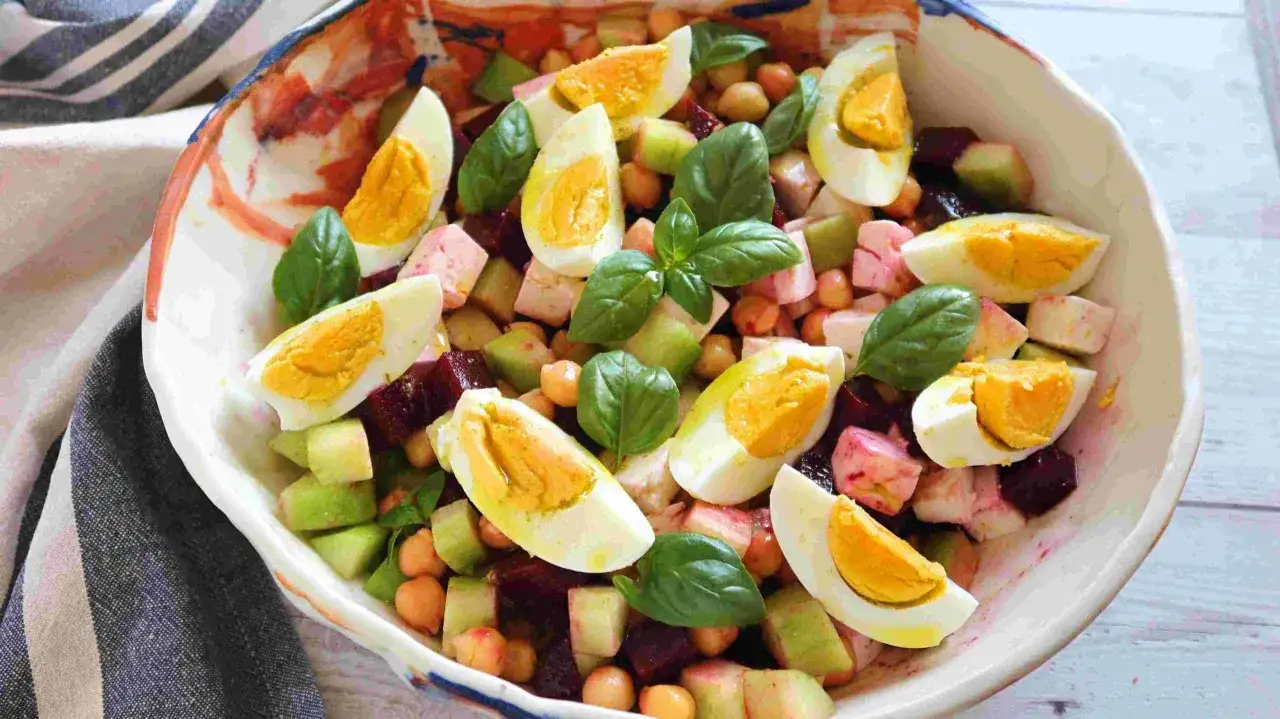 Ensalada de garbanzos con huevo duro, remolacha y manzana verde, decorada con hojas de albahaca fresca.
