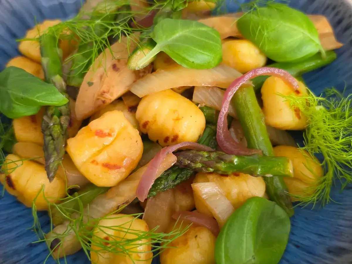 Gnocchi mit Spargel, Zwiebeln und frischen Kr&auml;utern in einer blauen Sch&uuml;ssel.