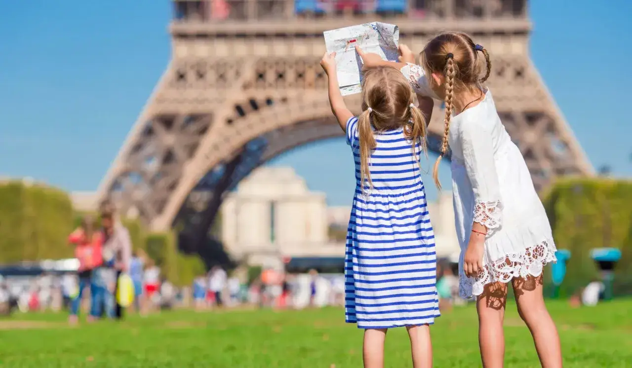 Dos ni&ntilde;as planean su aventura en Par&iacute;s, mapa en mano, frente a la Torre Eiffel. &iexcl;Ideas para que ver en Paris con ni&ntilde;os!