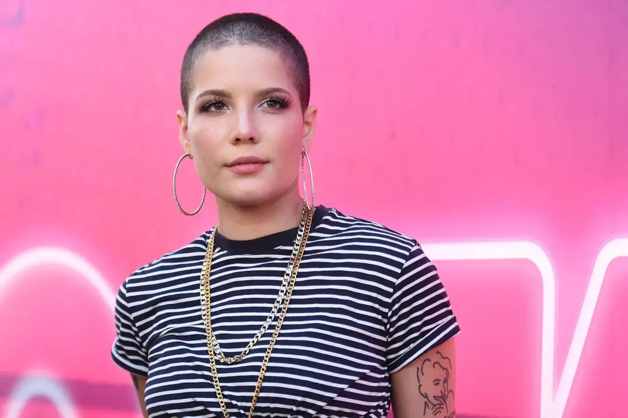Mujer con pelo rapado, aretes grandes y cadenas doradas, luciendo un estilo audaz.