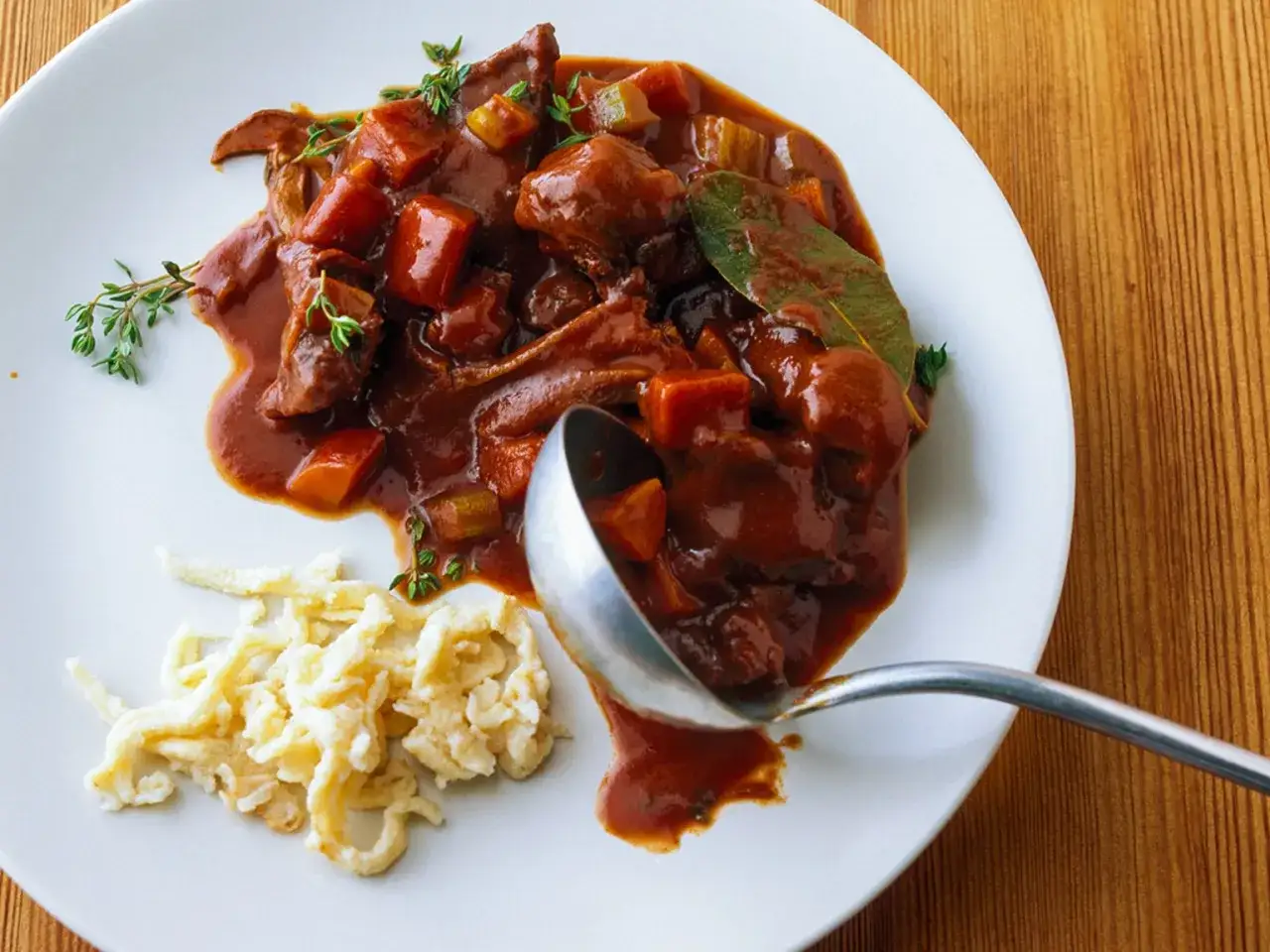 Herzhaftes Wildschwein Gulasch Rezept auf einem Teller mit Spätzle und frischen Kräutern, serviert mit einer Schöpfkelle.