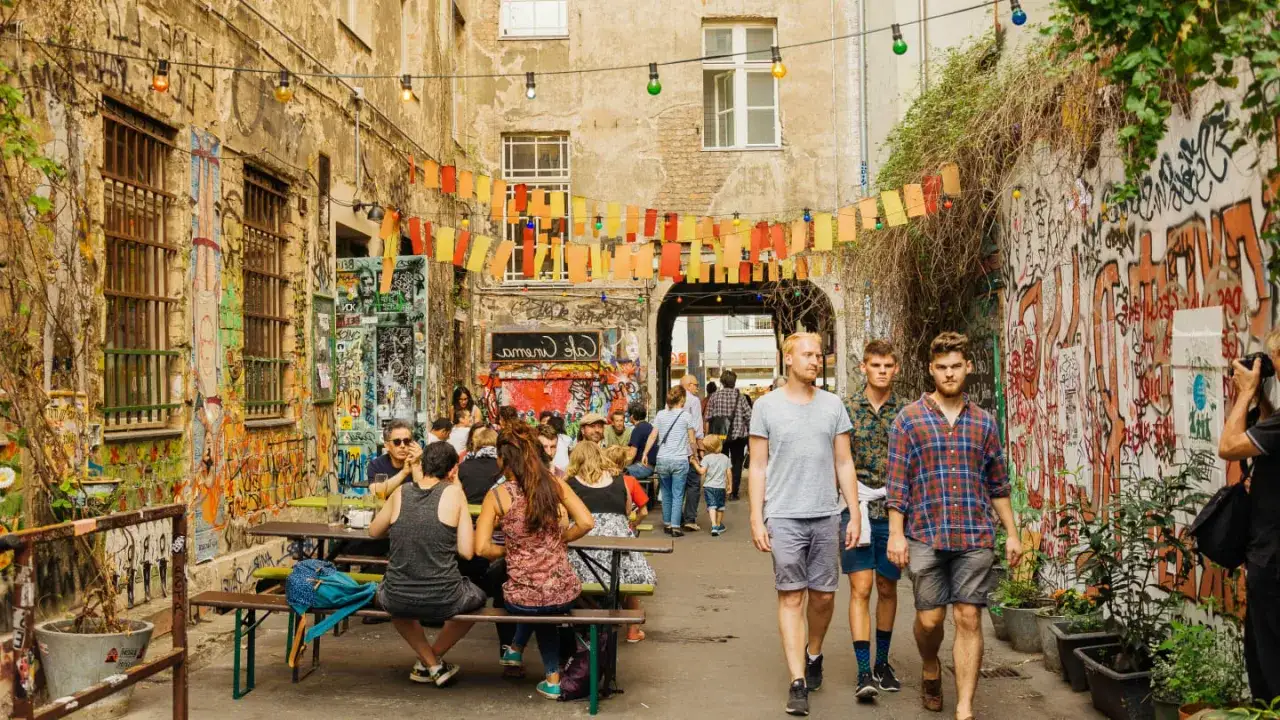 Bunte Lichterketten und Graffiti schm&uuml;cken einen belebten Innenhof in Berlin Kreuzberg. Menschen sitzen an Tischen, genie&szlig;en die Atmosph&auml;re.