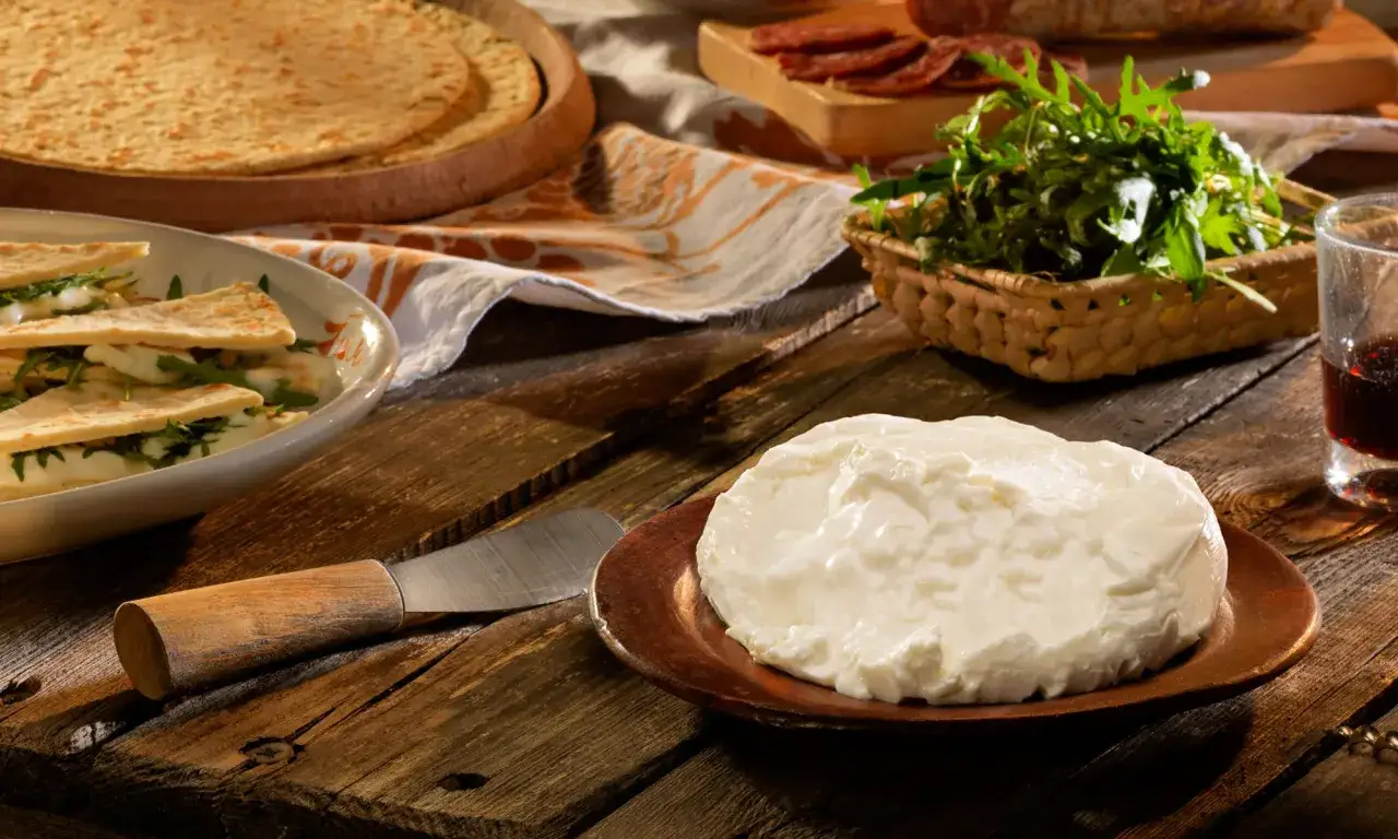 Un tavolo rustico pronto per degustazioni gastronomiche: formaggio fresco, focacce, rucola e salumi invitano a un assaggio.