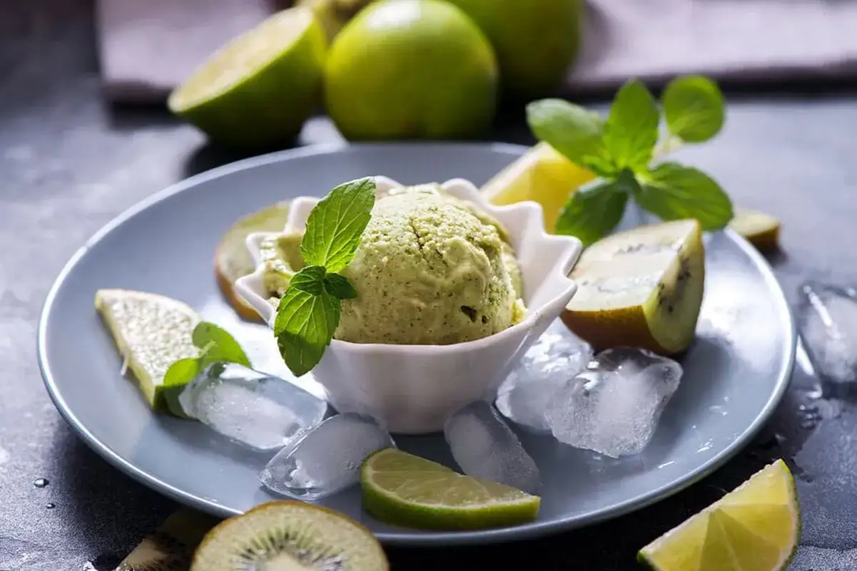 Erfrischendes Kiwi-Eis mit Minze, garniert mit frischen Kiwischeiben und Limettenspalten, serviert auf Eiswürfeln.
