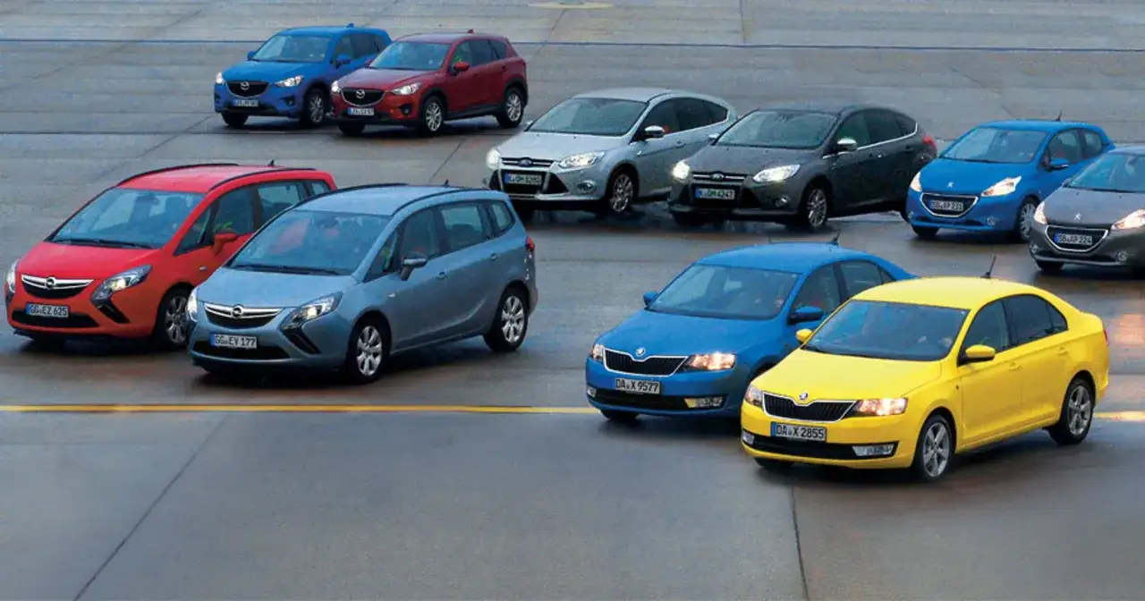 Różne modele samochodów, od kompaktowych po SUV-y, stoją na placu. Wybór między diesel czy benzyna jest trudny.