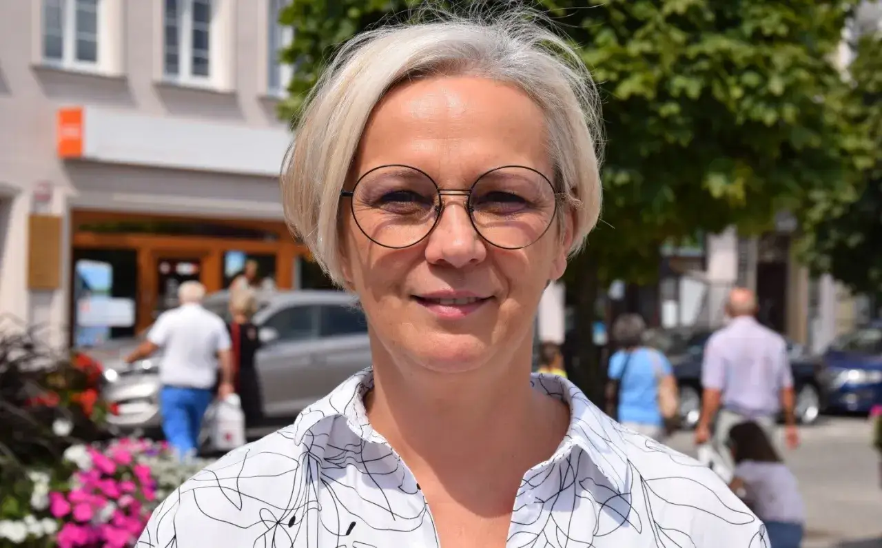 Dorota Niedziela, posłanka, w okularach i białej koszuli z czarnym wzorem, uśmiecha się na tle miejskiej ulicy.