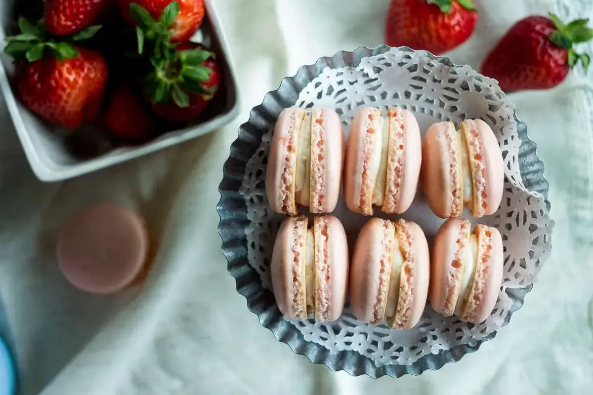 Różowe makaroniki z kremem, obok świeże truskawki. Idealne na deser.