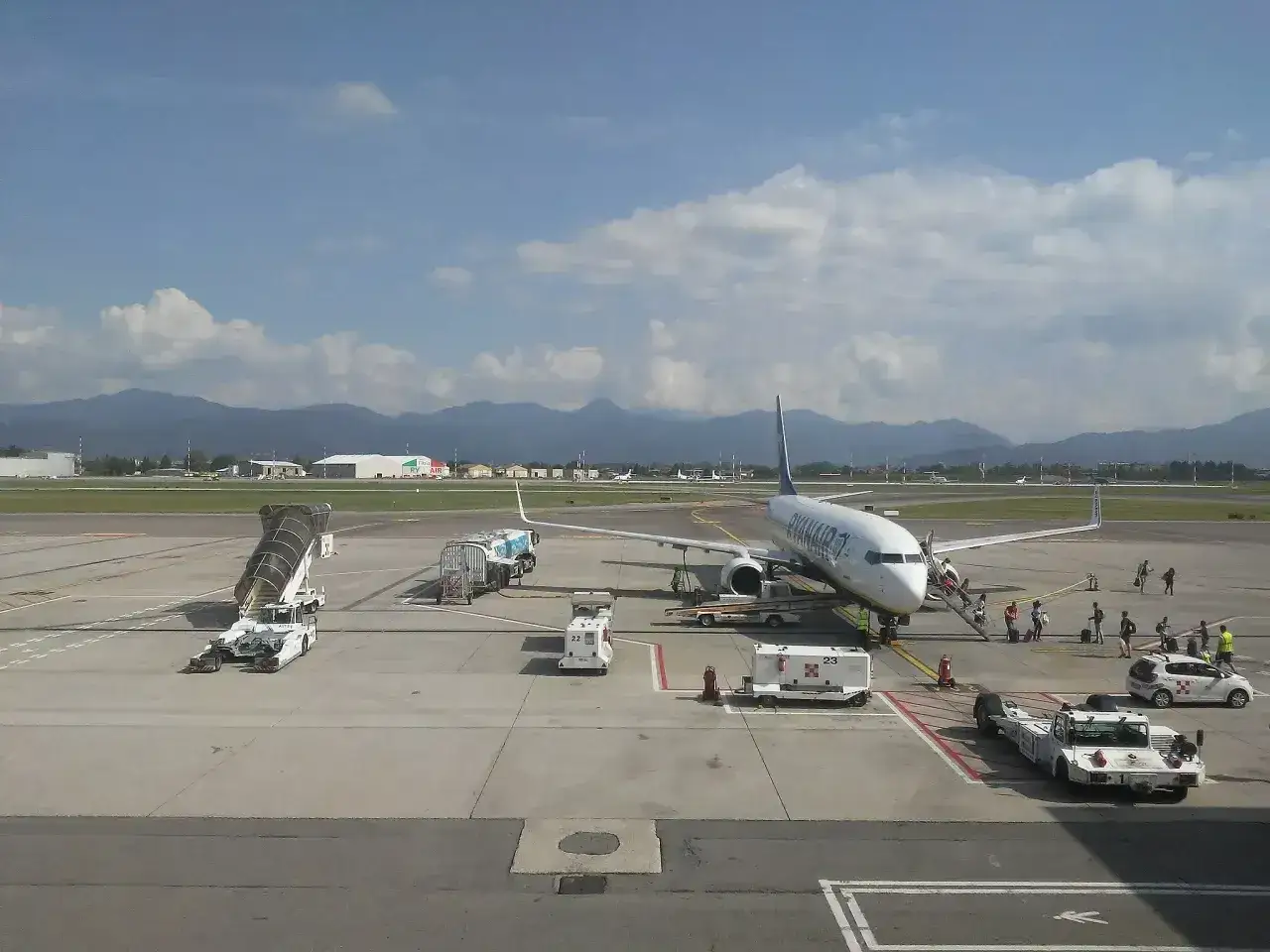 Samolot Ryanair na lotnisku Bergamo, pasażerowie wsiadają. W tle góry i budynki lotniska.