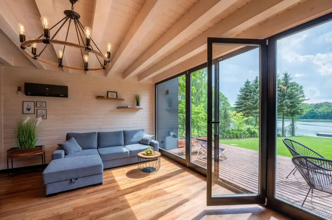 Przytulny salon w bungalow z widokiem na jezioro. Jasne drewno, wygodna sofa i duży taras zapraszają do relaksu.