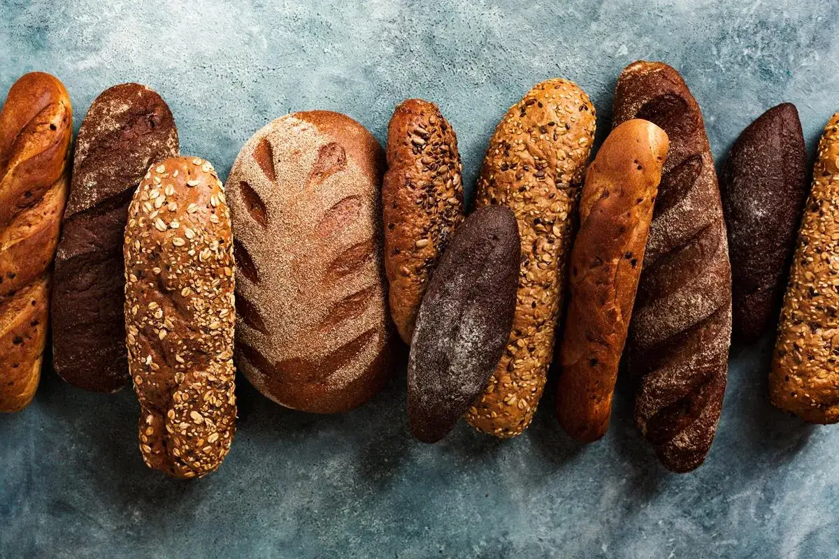 Różne rodzaje chleba: ciemny żytni, pszenny z ziarnami, bagietki i bochenki. Wybór dla każdego smakosza.