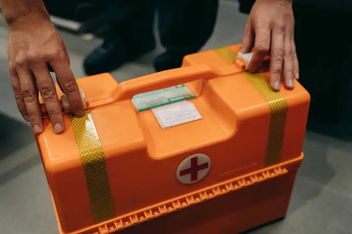 Mani che chiudono una cassetta medica arancione, pronta per un **infortunio sul lavoro risarcimento**.
