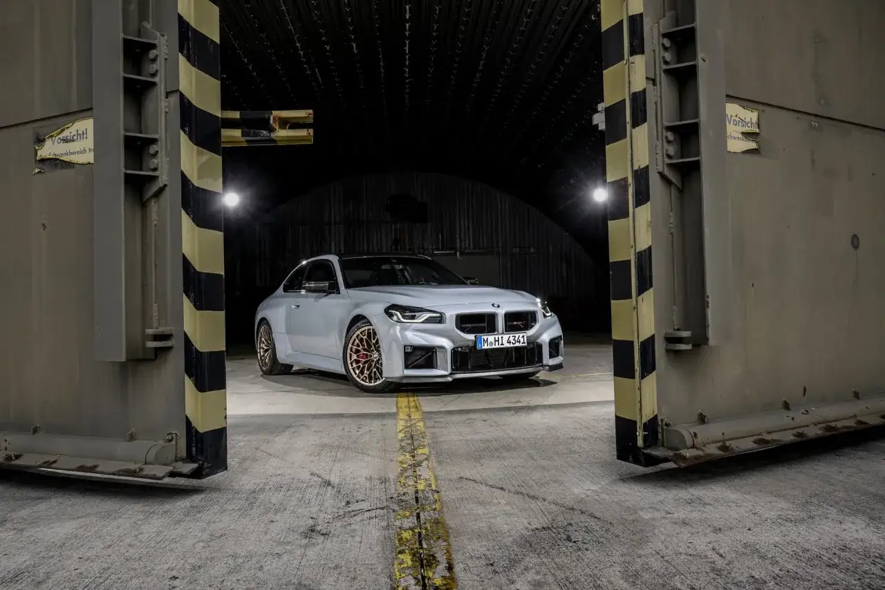 Srebrne BMW M2 G87 z brązowymi felgami stoi w otwartym hangarze.