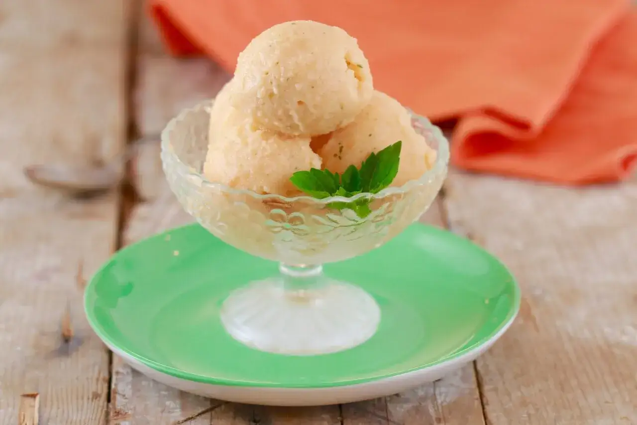 Erfrischendes Melonen Eis in einer Glasschale, garniert mit Minze, auf einem grünen Teller.
