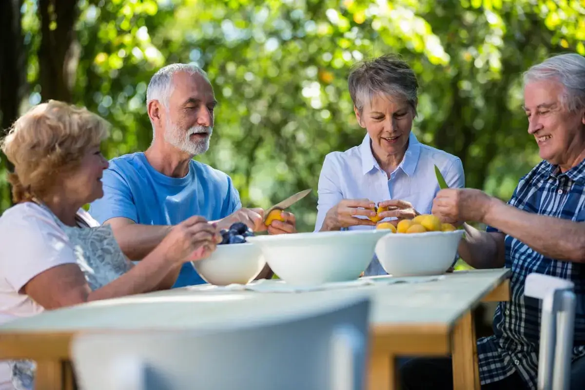 Czterech seniorów przygotowuje owoce na stole. Zdrowa dieta dla seniora po 80 roku życia to klucz do dobrego samopoczucia.