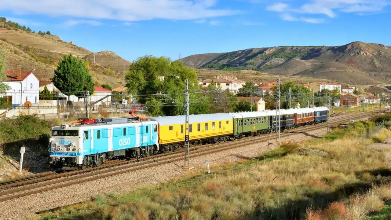 Un tren de Alsa, con su locomotora azul y blanca, avanza por la vía. Los vagones de colores, amarillo, verde y azul, transportan pasajeros en su viaje de Zaragoza a Logroño.