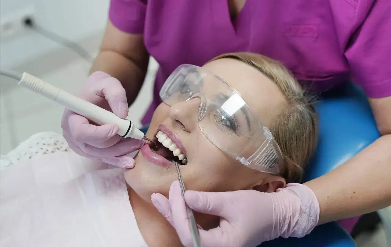 Pacjentka w okularach ochronnych przechodzi zabieg usuwania kamienia nazębnego. Dentysta delikatnie oczyszcza jej zęby.