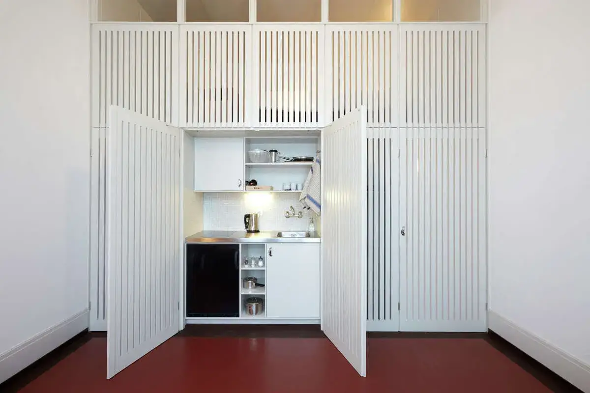Cocina sin encimera, oculta tras puertas blancas. Incluye fregadero, placa de inducci&oacute;n y mini-nevera.