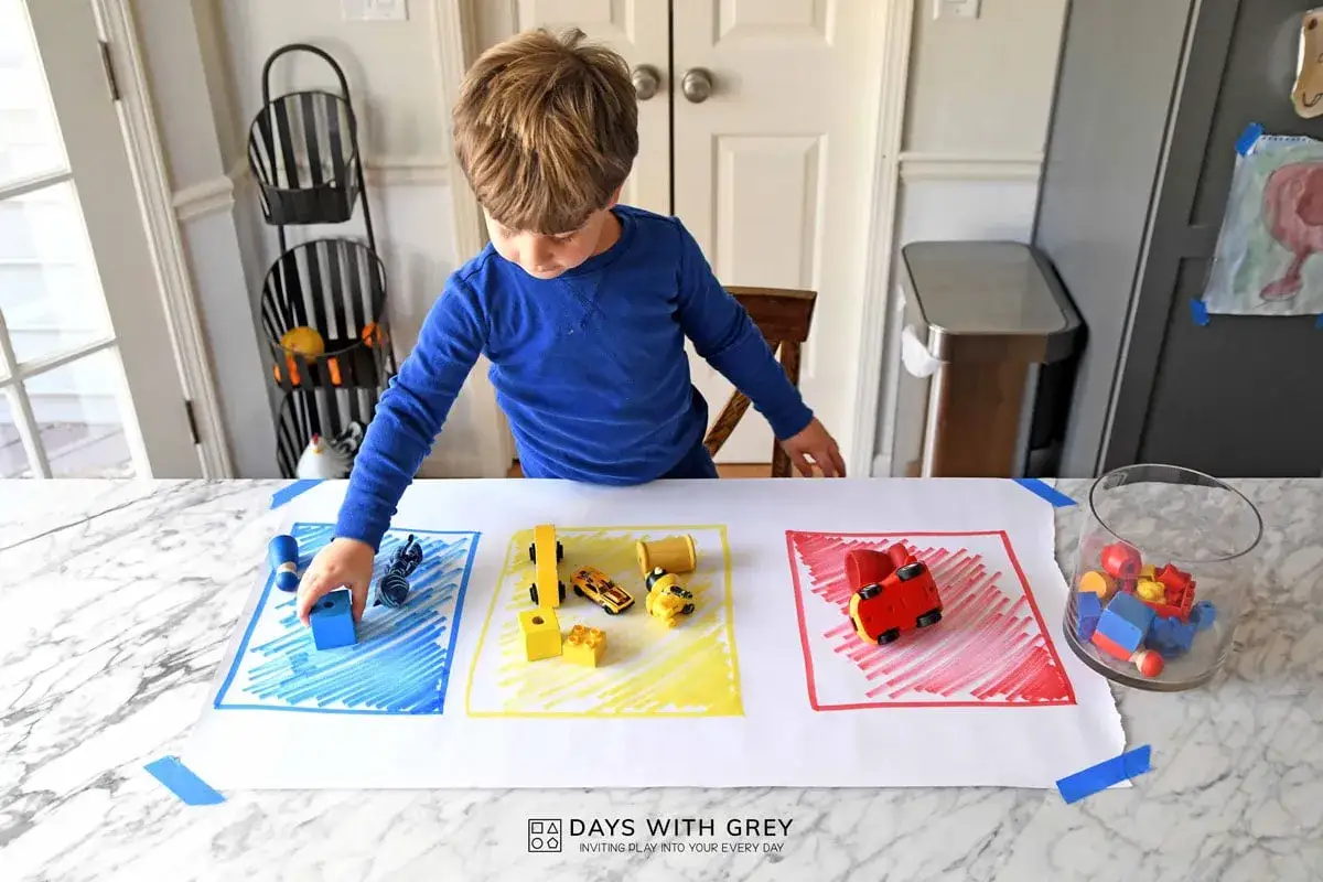 A boy sorts blue, yellow, and red toys on a paper mat, learning colors for his 1 year old birthday.