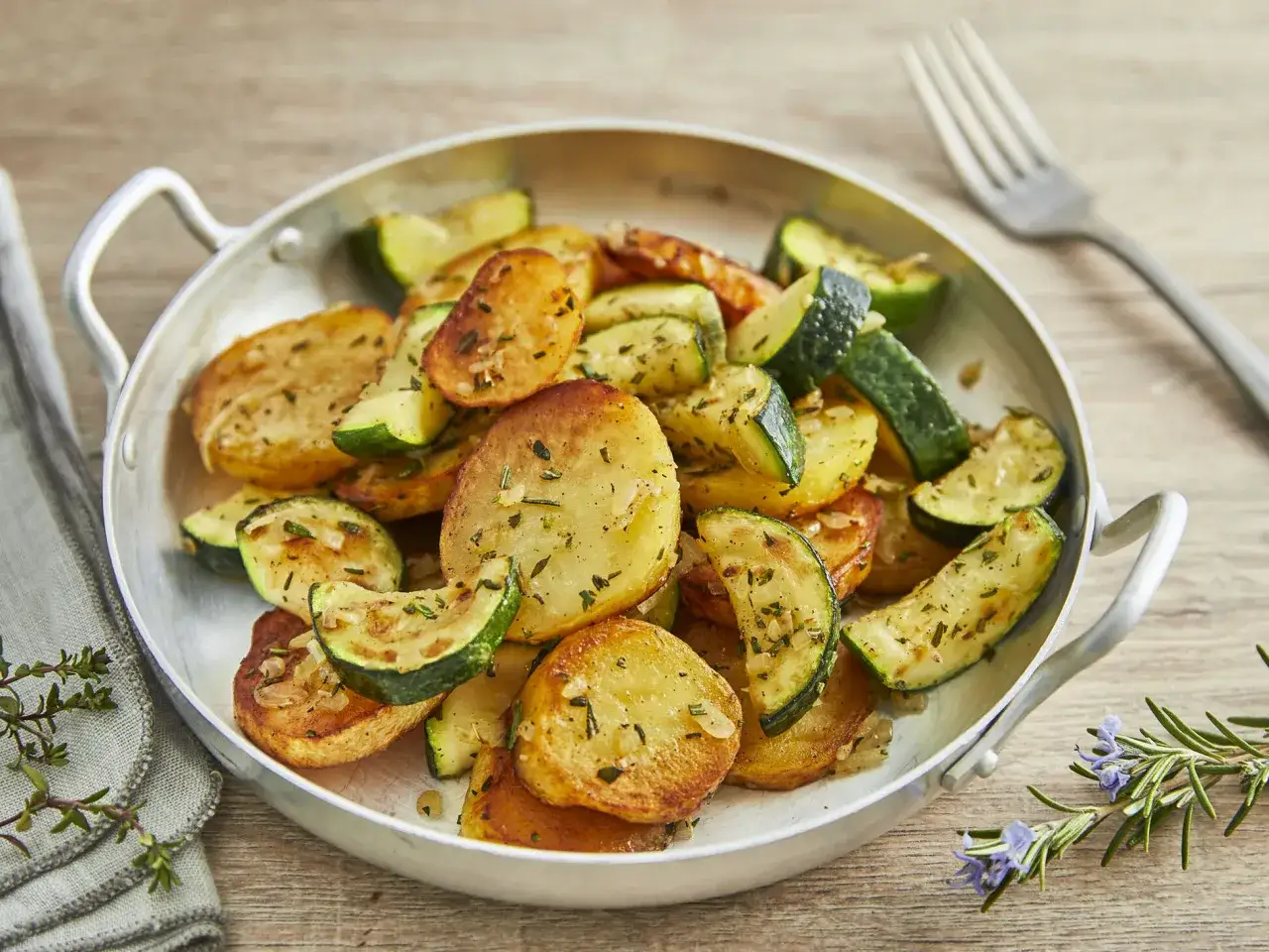 Herzhafte zucchini pfanne mit goldbraunen Kartoffelscheiben und Kräutern, serviert in einer Metallpfanne.