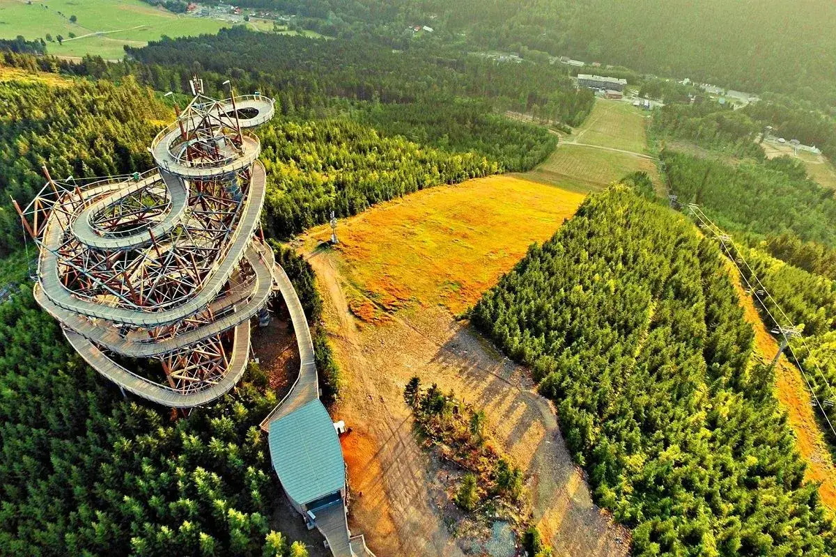 Widok z lotu ptaka na spiralny wiszący most w Czechach, otoczony lasem i złotym polem.
