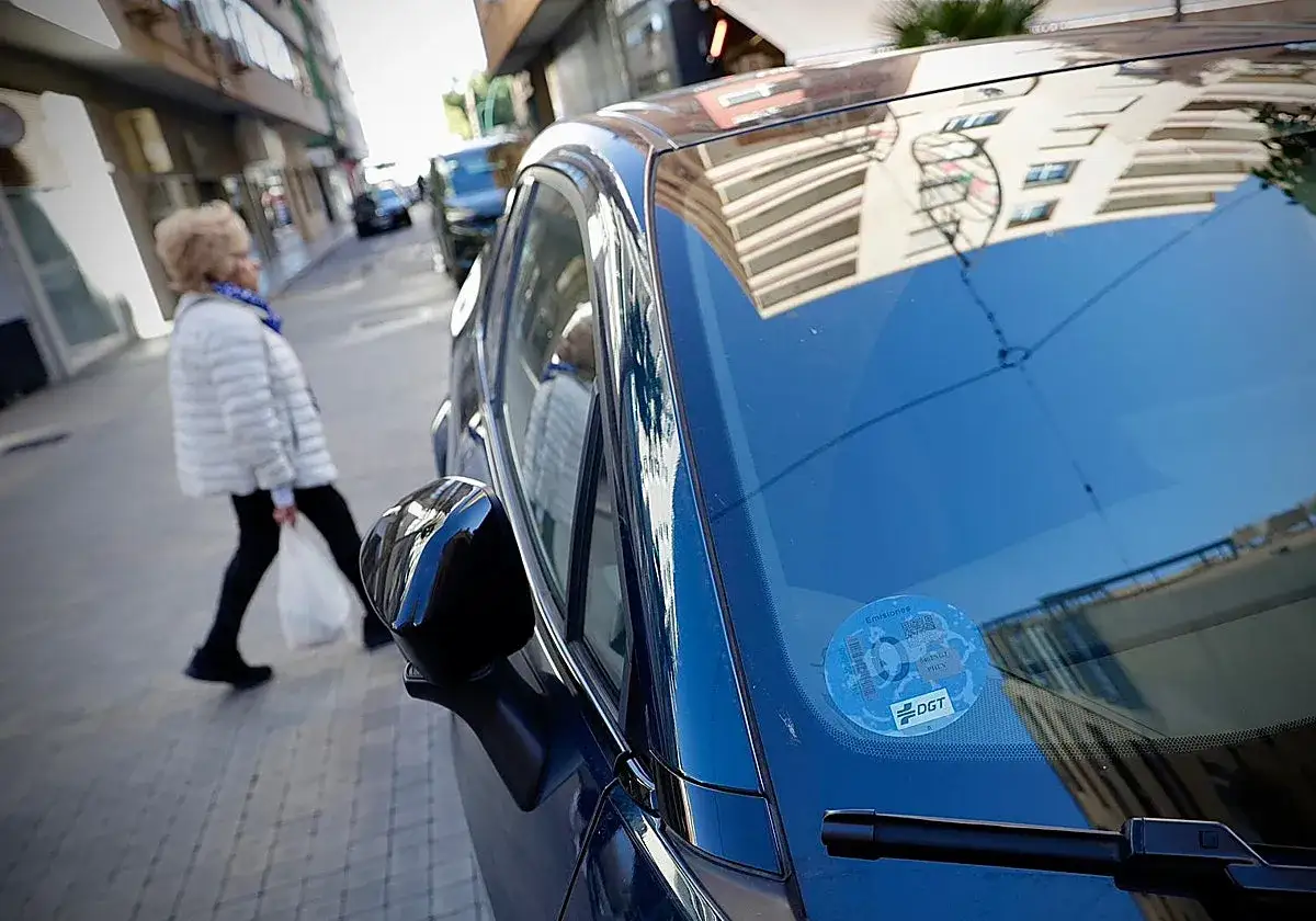 Una mujer cruza la calle mientras un coche eléctrico, con pegatina DGT, espera. Los coches eléctricos pagan zona azul.