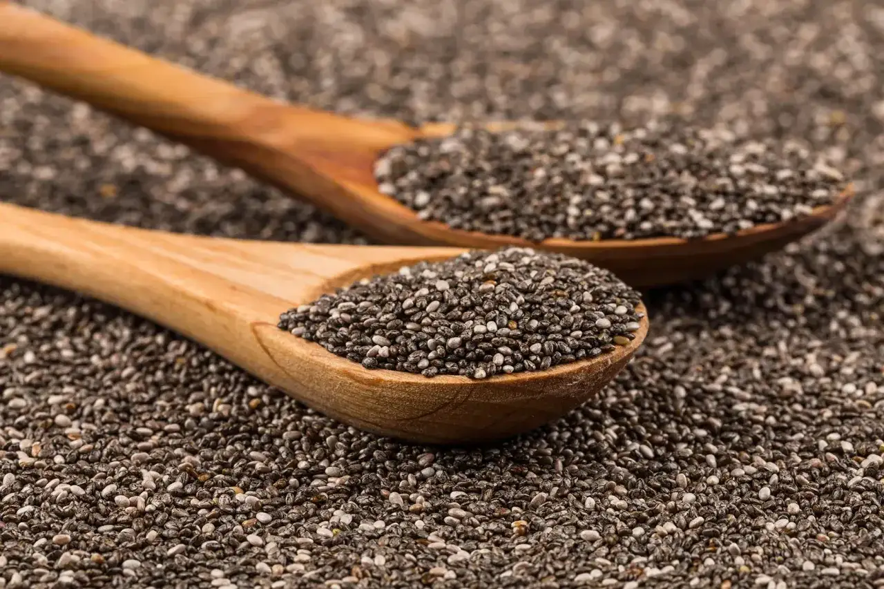 Due cucchiai di legno pieni di semi di chia, un aiuto naturale per sgonfiare la pancia.