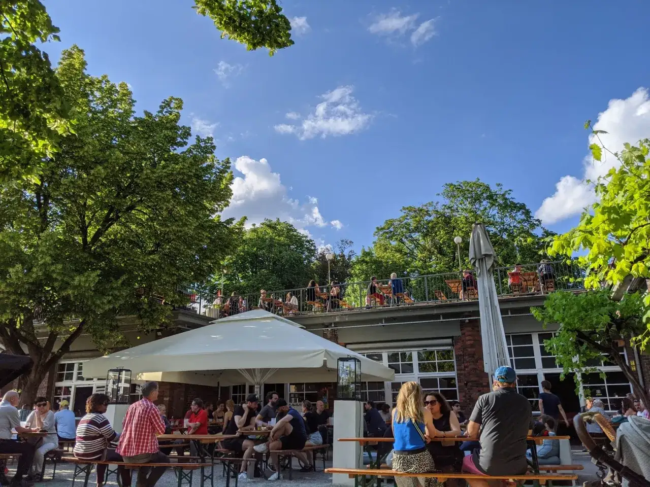 Menschen genie&szlig;en das Wetter im Golgatha Biergarten unter B&auml;umen.