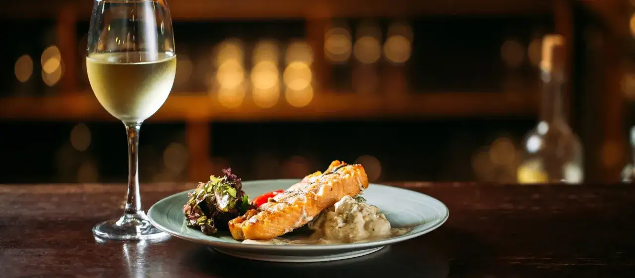 Un plato de salmón a la parrilla con ensalada y una copa de vino blanco, perfecto para un maridaje con riesling.