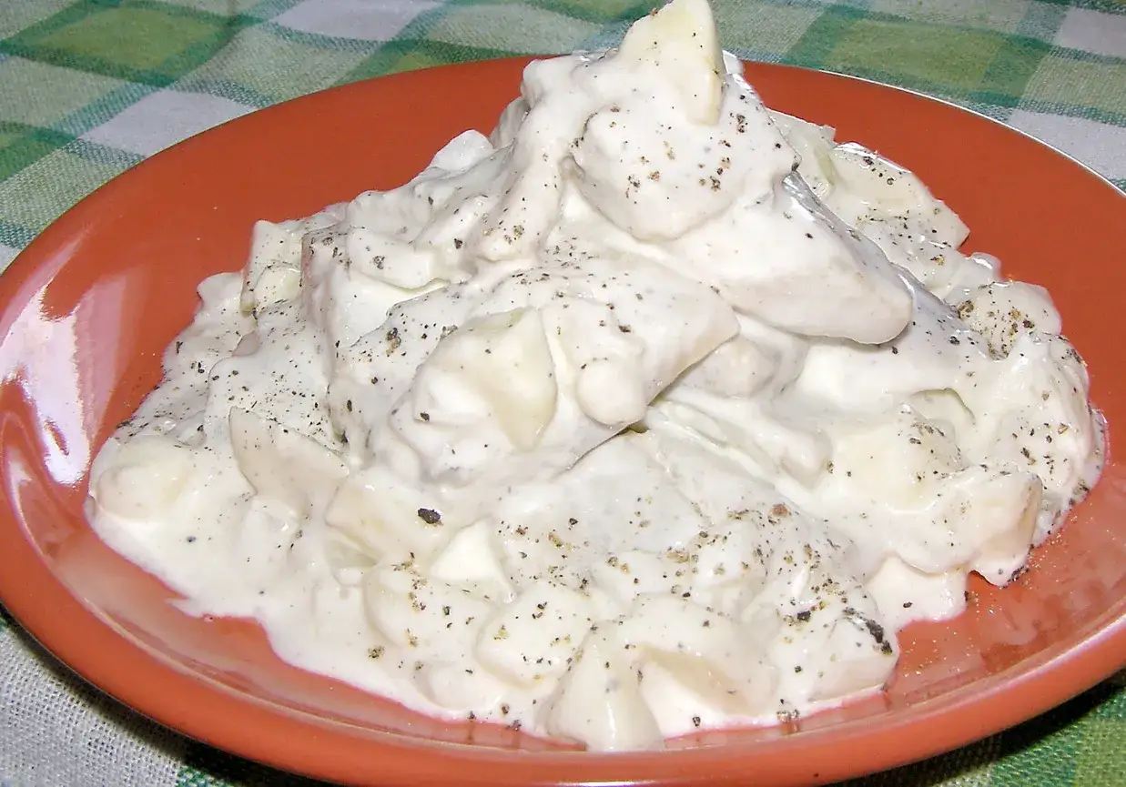 Pyszne śledzie w śmietanie, doprawione pieprzem, podane na pomarańczowym talerzu.