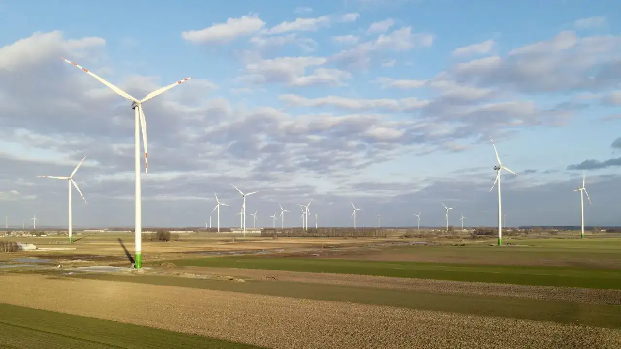 Rozległe farmy wiatrowe na tle błękitnego nieba z chmurami. Wiatraki obracają łopatami, czerpiąc energię z wiatru.