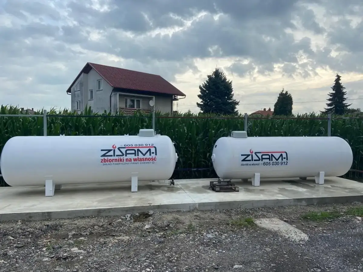Dwa białe zbiorniki na propan stoją na betonowej podstawie. Zapewniają one własne źródło gazu.