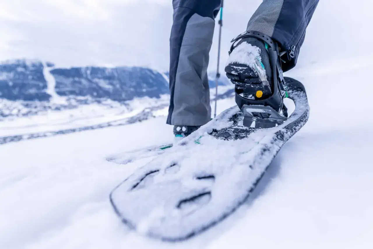 Piede con racchette da neve che affonda nella neve fresca, pronto per camminare in montagna.