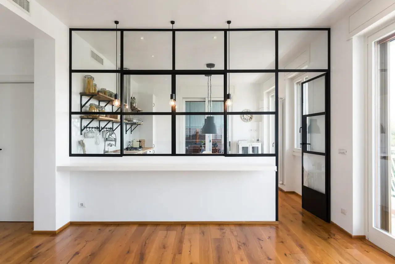 Moderna separacion pared cristal cocina salon con estanterías y encimera blanca.