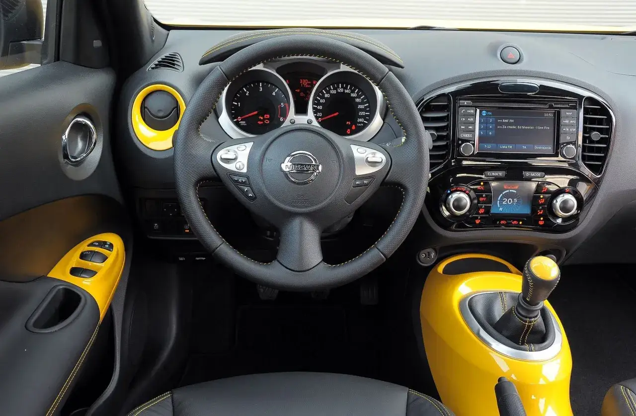 Wnętrze Nissan Juke 1.6 benzyna z żółtymi akcentami. Kierownica, deska rozdzielcza i dźwignia zmiany biegów.