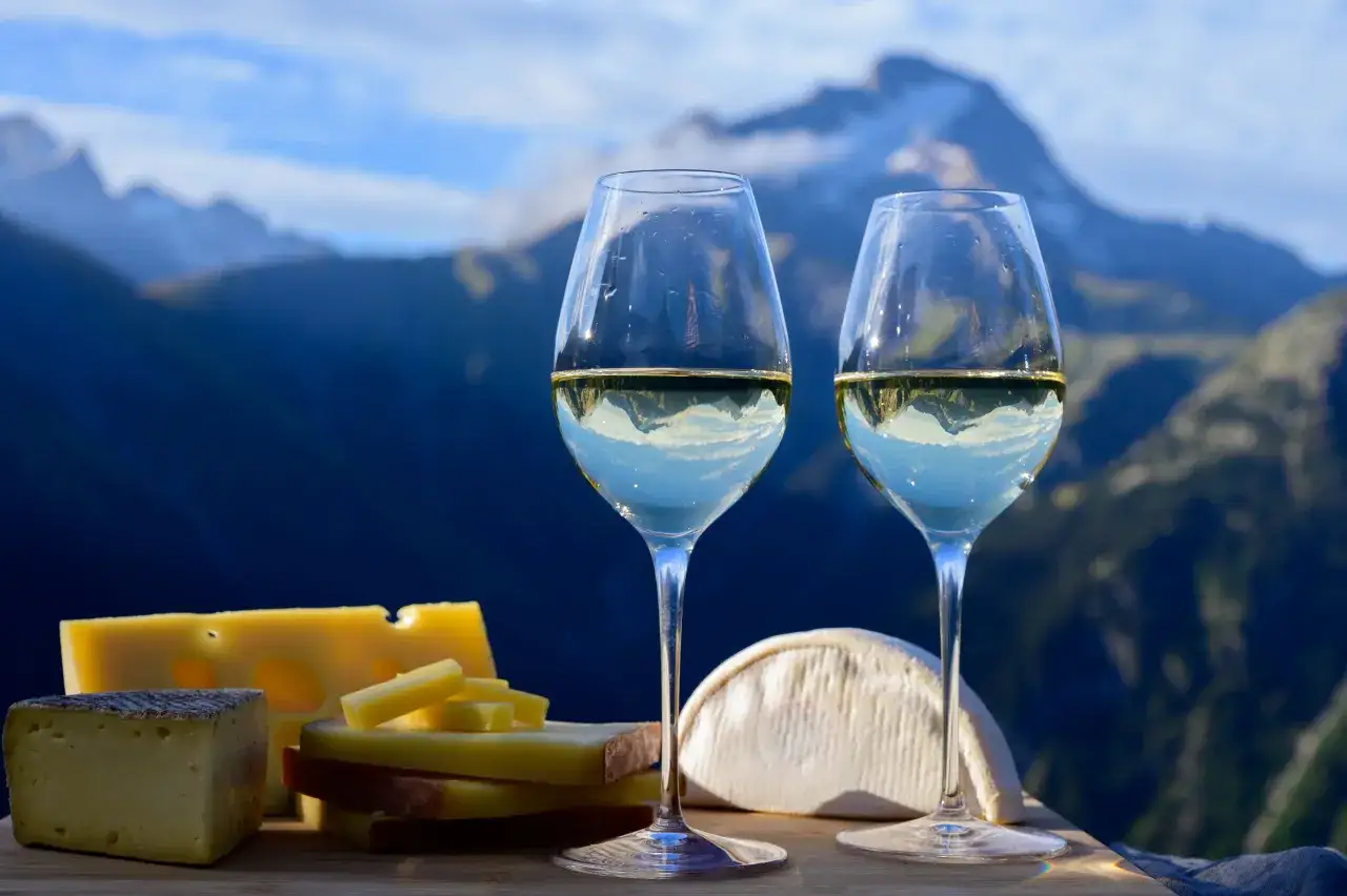Deux verres de vin blanc sec ou moelleux, parfaits pour accompagner une raclette, avec des montagnes en arrière-plan.