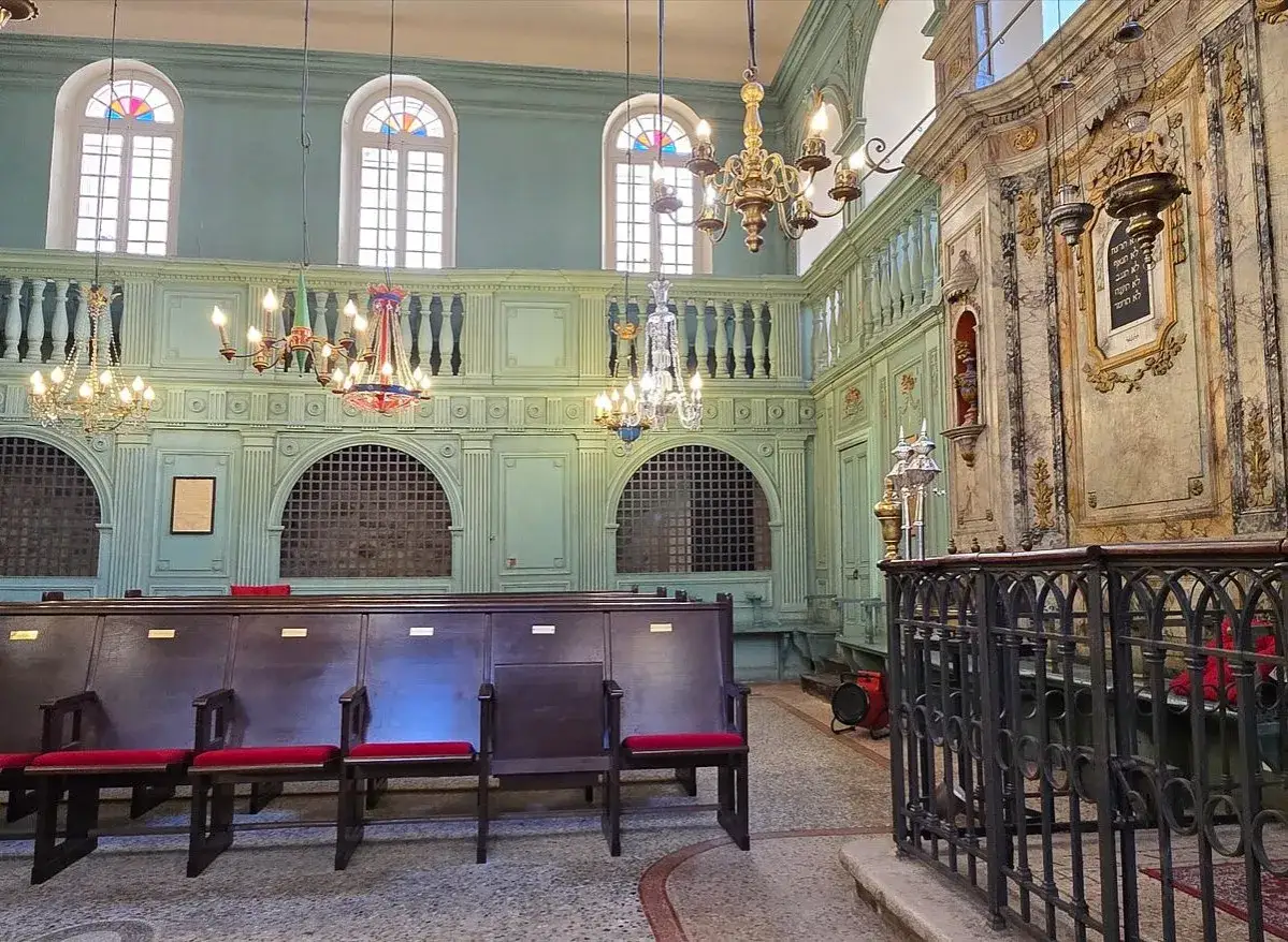 Intérieur d'une synagogue ornée, avec des bancs en bois, des lustres anciens et des fenêtres cintrées. Un lieu de visite incontournable pour le tourisme à Carpentras.
