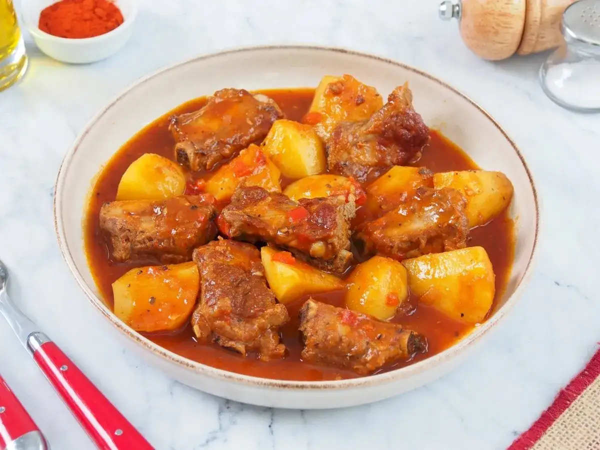 Un plato humeante de costillas guisadas con patatas, cubiertas de una rica salsa roja.